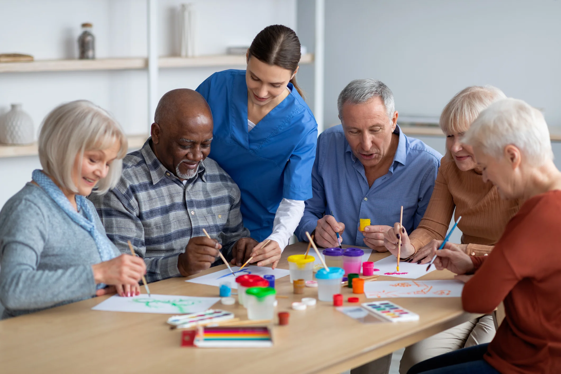 Group home residents enjoying a creative painting activity together with a caregiver supervising