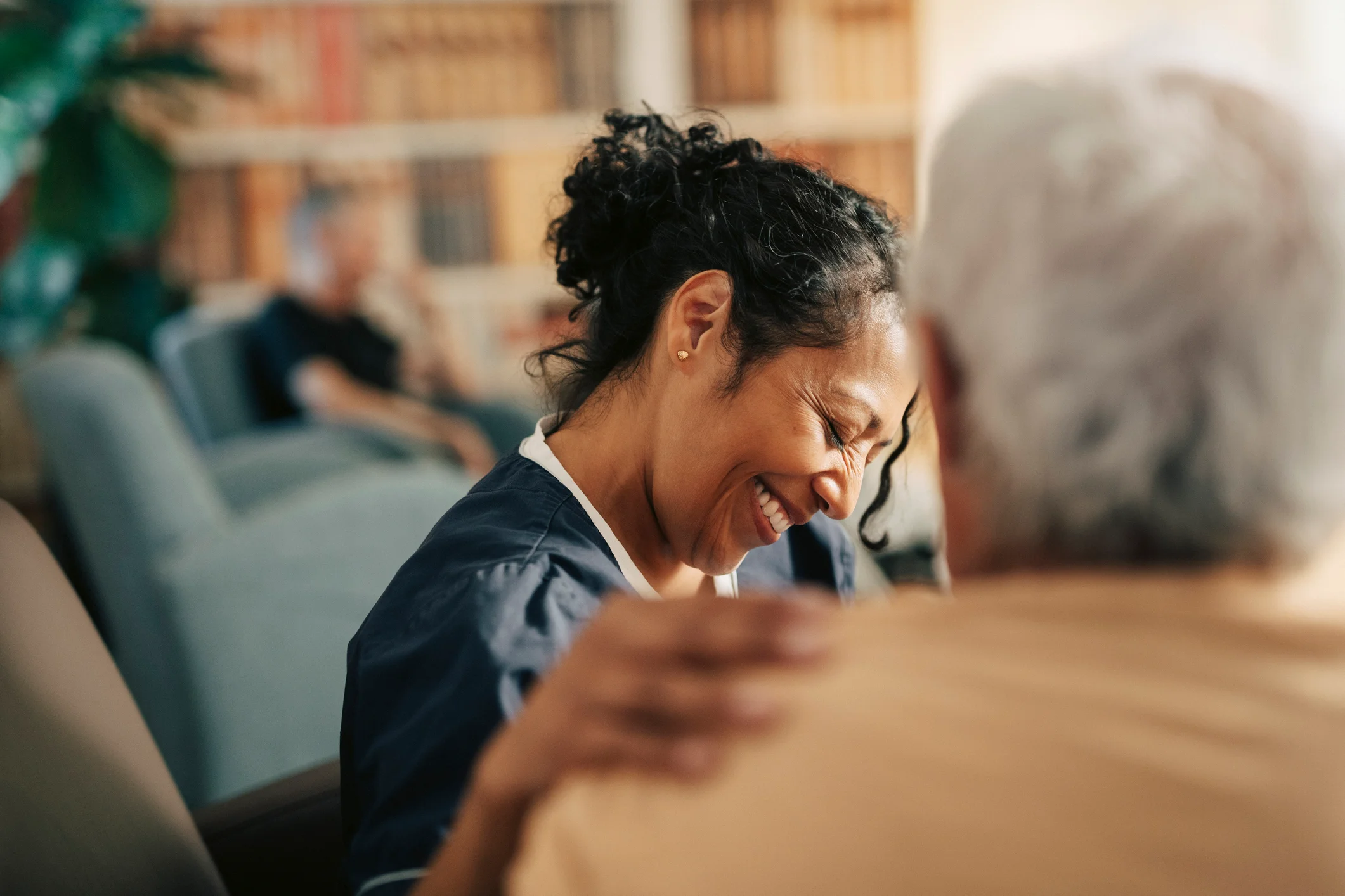 Compassionate nursing home caregiver smiling while comforting an elderly resident in a care facility common area