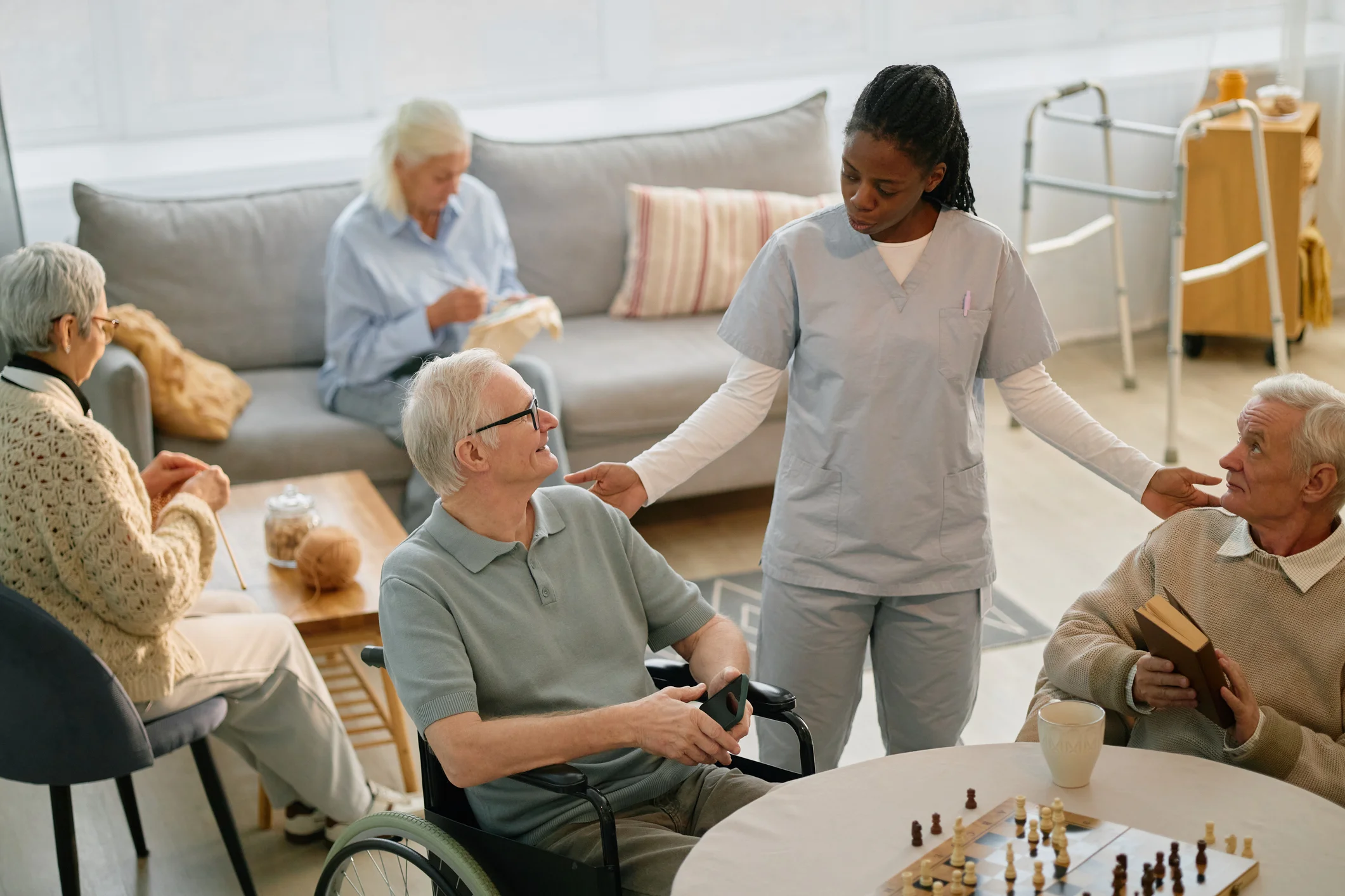 Skilled nursing facility staff assisting residents in wheelchairs during a social activity in the common room