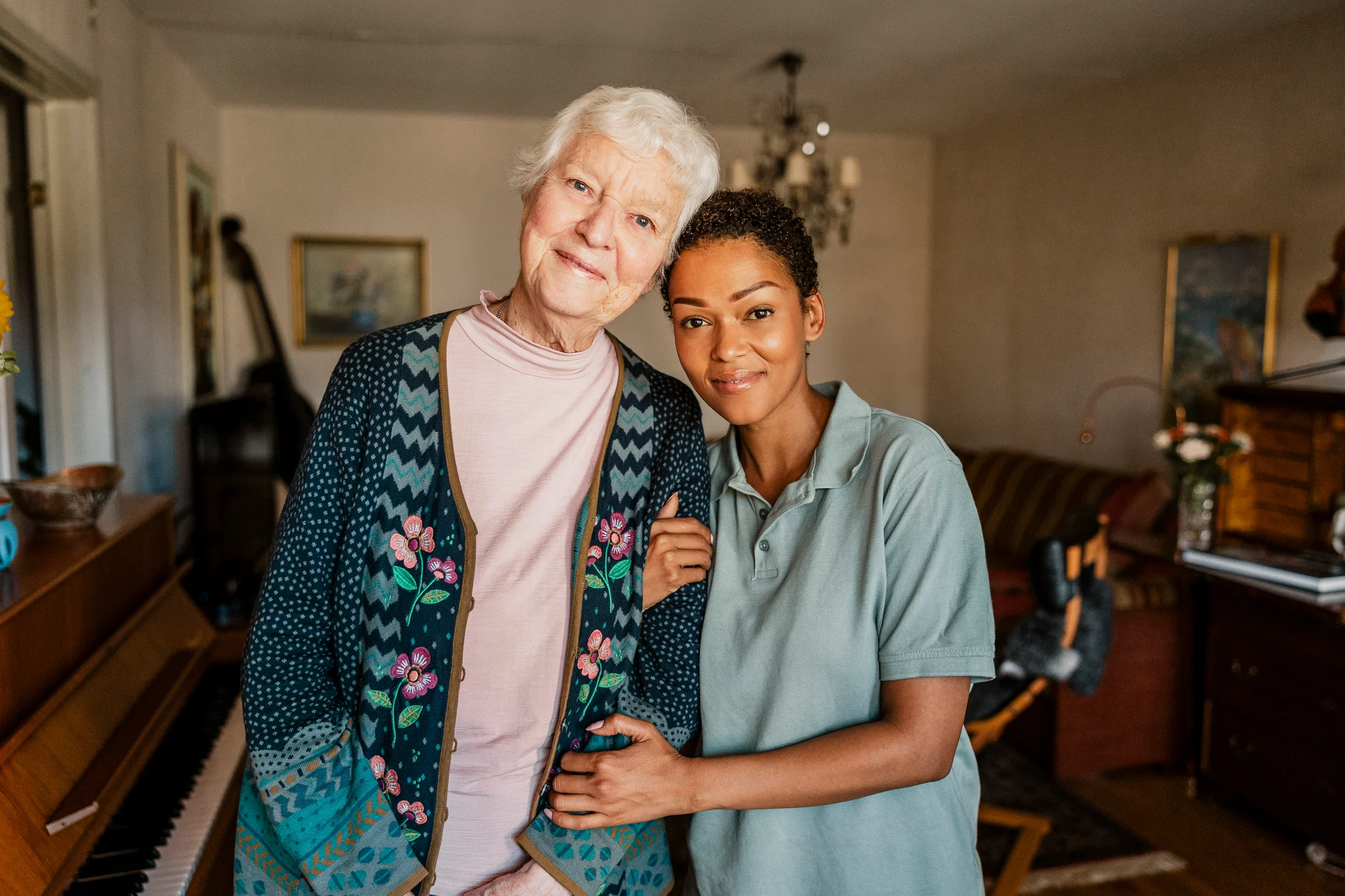 Elderly woman and caregiver standing together in a warm, sunlit home — compassionate senior care